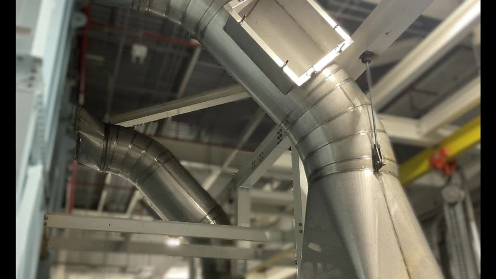Overhead industrial galvanized ductwork junction with multiple branch connections and cone reducers inside a facility